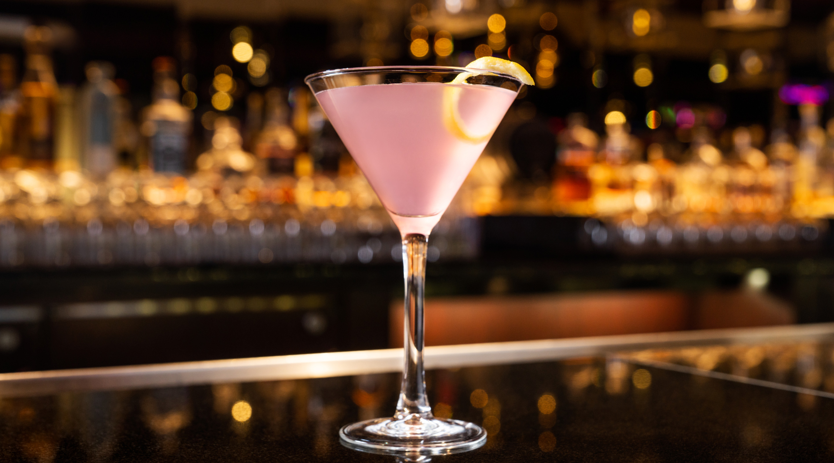 A Lavender Pearl Martini with a lemon peel garnish on a bar.