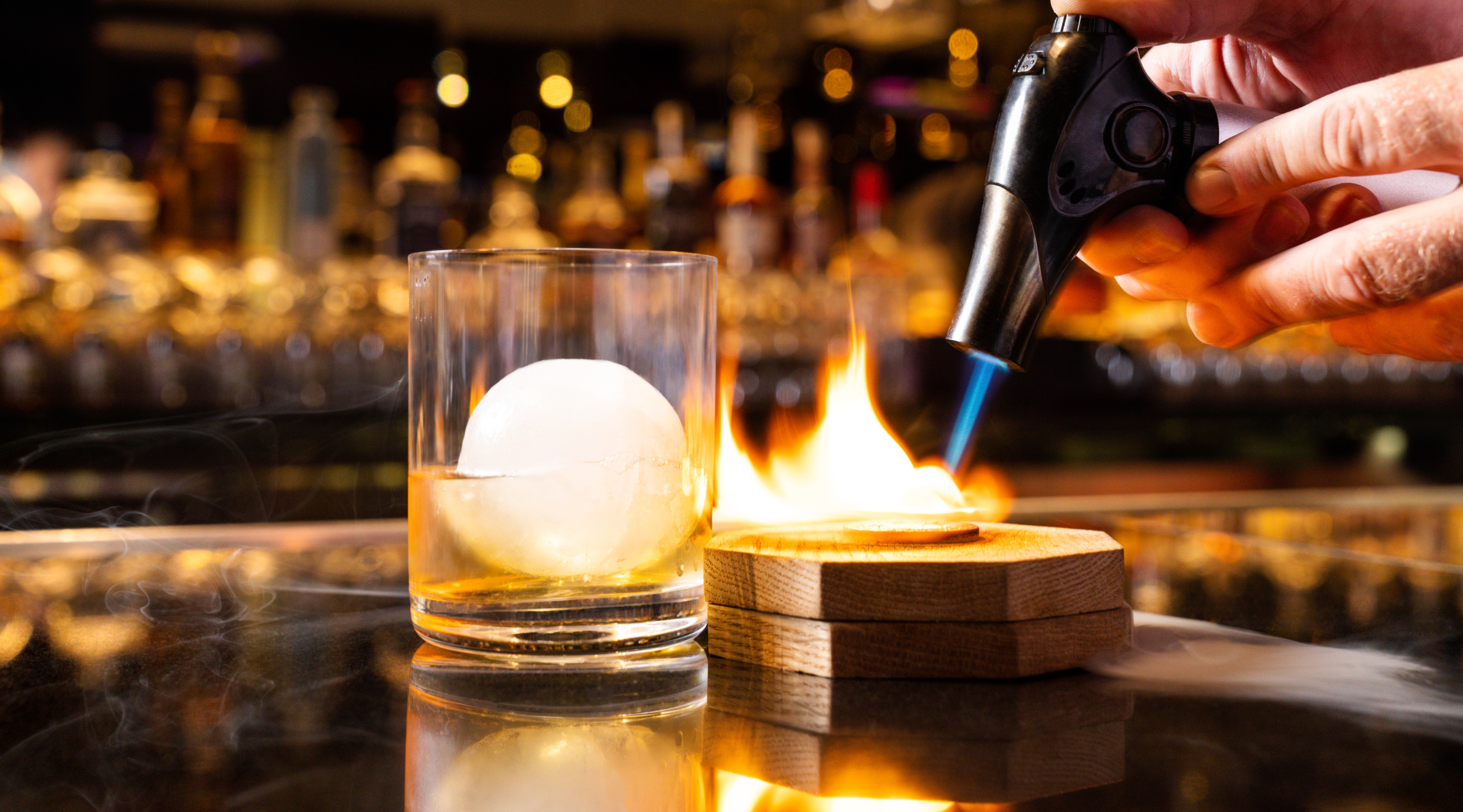 A smoked Old Fashioned cocktail with a circular ice cube in a rocks glass.